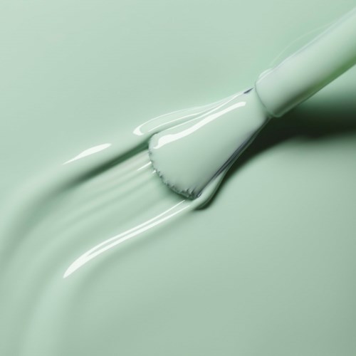 A brush spreading mint green paint smoothly on a surface.