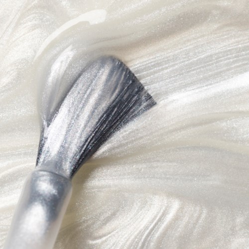 A makeup brush spreads white powder or cream on a smooth surface.