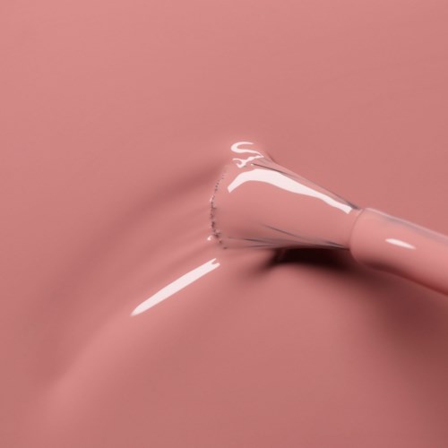 A pink beauty blender sponge is pressed into a pink surface, creating a splash-like effect with some liquid.