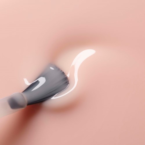 A makeup brush is applying white cream or foundation on skin.
