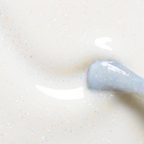 A tube of white paint is squeezing out paint onto a white surface with colorful small specks.