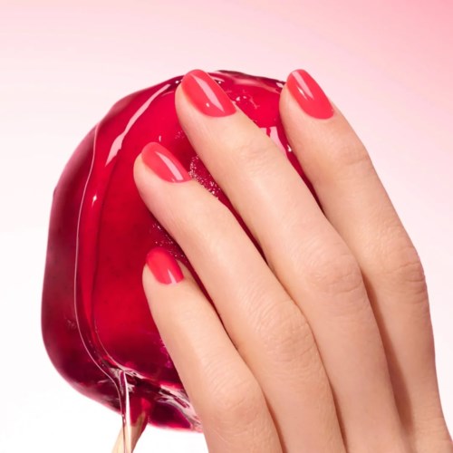 A hand with red painted nails touches a shiny red heart-shaped object.