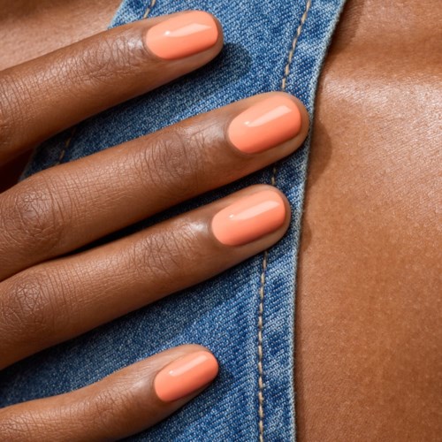 Close-up of a hand showing peach-colored nails resting on blue denim fabric.