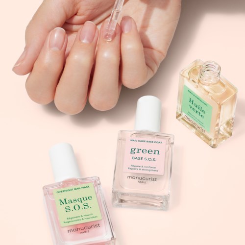 Iemand brengt heldere nagelolie aan met een druppelaar, met drie flessen nagelproducten dichtbij op een lichte ondergrond.