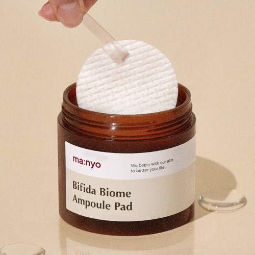 Een bruine pot gelabeld 'Bifida Biome Ampoule Pad' met een witte pad die wordt geplaatst met een stok.