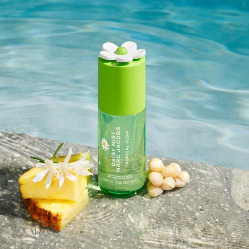 A green spray bottle with a white daisy flower cap, placed on a stone beside pineapple and white stones, by water.