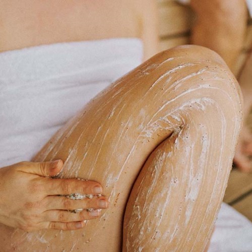 A person is applying a clay mask or similar substance to their leg in a spa or bath setting.