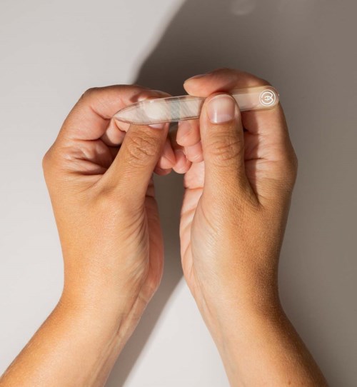 Person holds a small transparent device or object with both hands, positioned against a plain background.