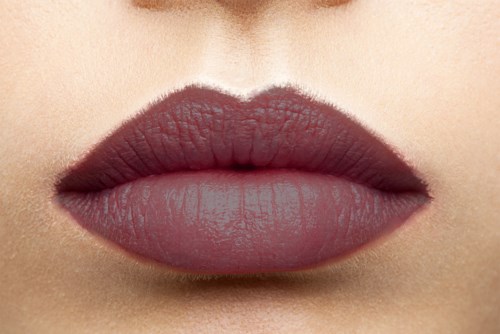 Close-up of lips with dark lipstick and smooth skin, with some shadows for depth.