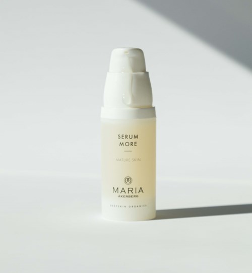 Een witte fles huidverzorgingsserum met 'Maria Ackermann' en 'Serum More'. Zonlicht werpt schaduw.