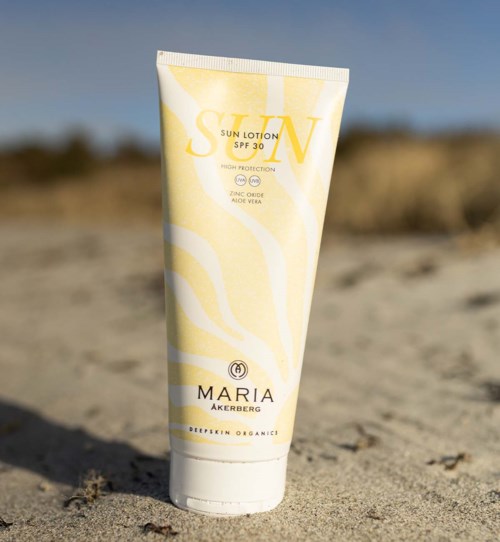 Een tube zonnebrandcrème met SPF 30 op het zand met een heldere hemel op de achtergrond.