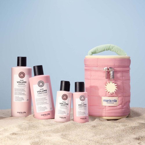 Vier pinke Flaschen mit Haarprodukten und eine kleine pinke Tasche mit grünem Griff liegen im Sand.