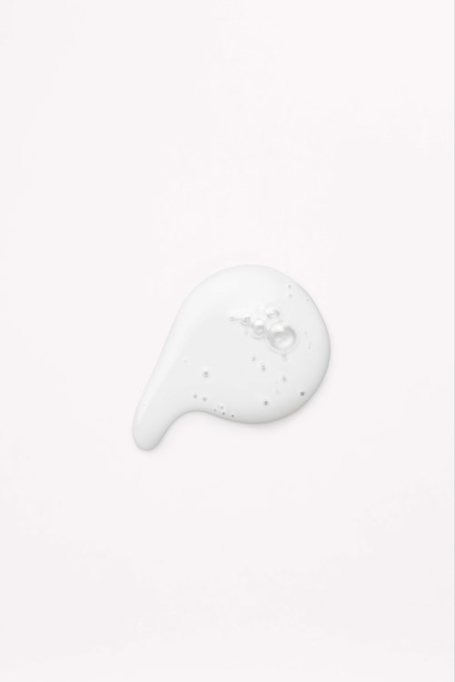 Eine kleine Menge weiße Lotion oder Creme ist auf einer weißen Oberfläche verteilt. Es hat eine glatte, leicht glänzende Textur.