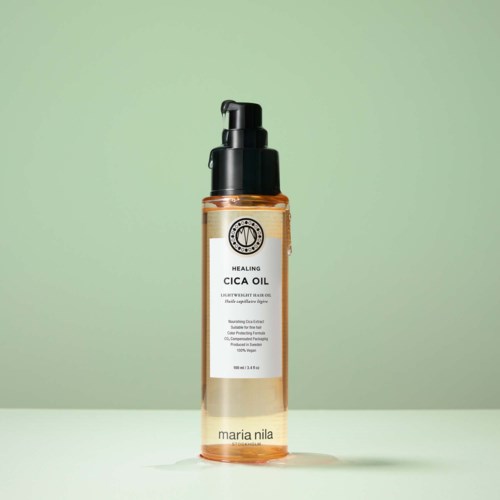 A clear bottle of healing cica oil with a pump top on a green background.