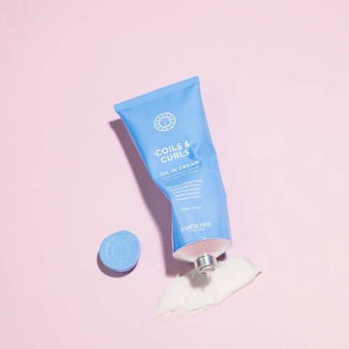A blue tube of hair styling cream with its cap off, spilling some cream on a pink background.