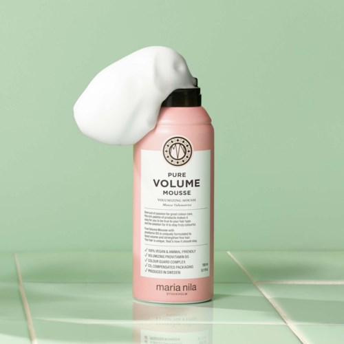 A pink can of volumizing mousse with a white foam puff on top, placed on a tiled surface.