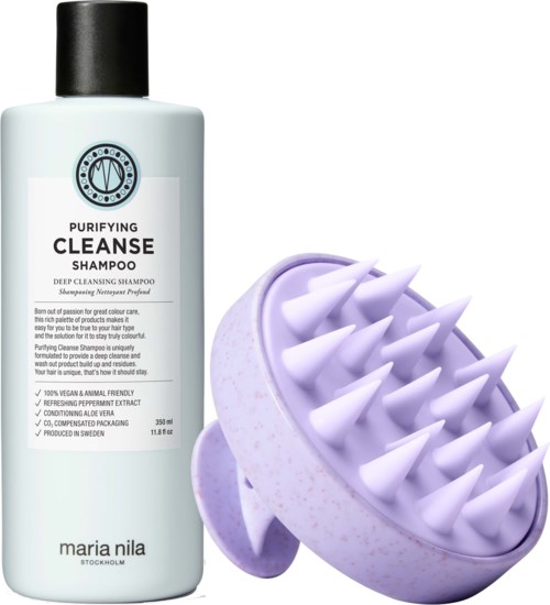 A white bottle of cleansing shampoo with black cap, next to a purple scalp massager with spikes.