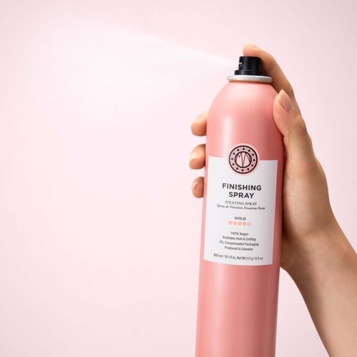 En hand håller en rosa sprayflaska märkt Finishing Spray som sprutar ut en fin dimma mot en ljus bakgrund.