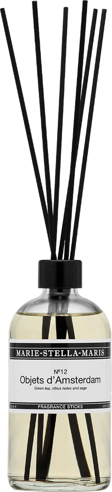 A glass bottle with black sticks inside, labeled Objets dAmsterdam, releasing fragrance into the air.