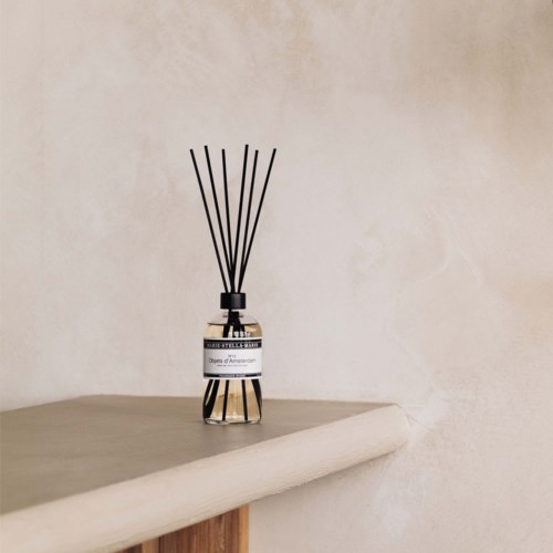 A black and white reed diffuser with sticks on a plain surface against a light wall.