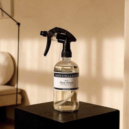Een heldere sprayfles met een zwart trekskelet staat op een donkerhouten oppervlak, gemarkeerd Rock Roses door Marie-Stella-Maris.