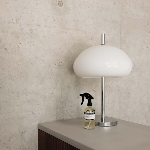 Een witte lamp en een sprayfles staan op eengrijze oppervlak tegen een textuur muur.