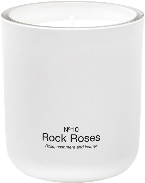 En enkel vit doftljus med svart text som heter Rock Roses, doftsatt med ros, cashmere och läder.