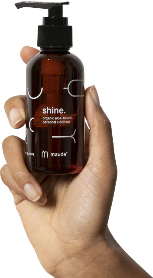Eine Person hält eine braune Flasche mit Pumpe. Das Etikett lautet 'shine.' und erwähnt organische Aloe-Basis.