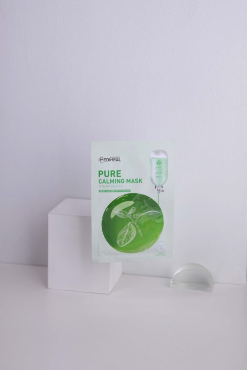En ansiktsmaskförpackning i grönt och vitt, placerad på en vit yta med enkel bakgrund.