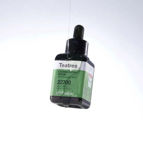 Een pipet boven een zwarte fles Teatree kalmerend serum met Hyaluronzuur, etiket bevat productinformatie.