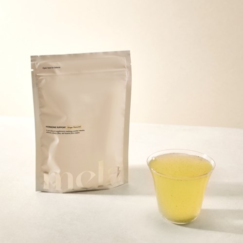 A silver bag with text and a clear glass cup filled with yellow liquid on a white surface.