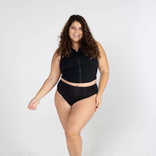 Eine glückliche Frau in schwarzer Sportkleidung steht vor einem schlichten weißen Hintergrund.