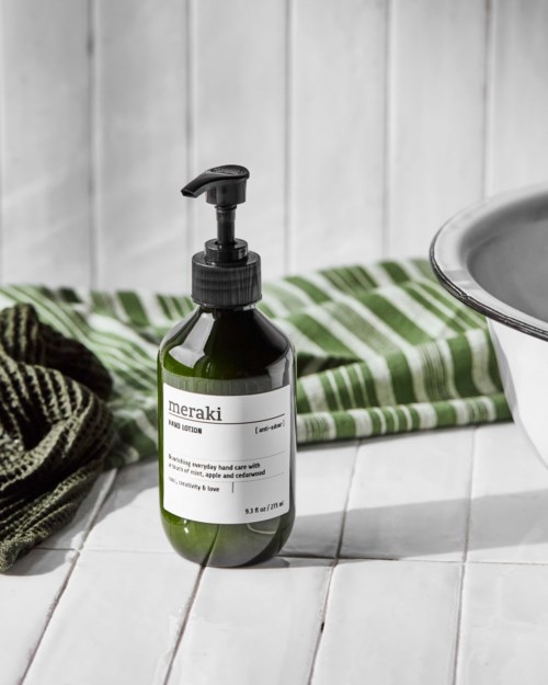 Een groene fles handzeep met pomp, naast een wastafel en een groen-gestreepte handdoek.
