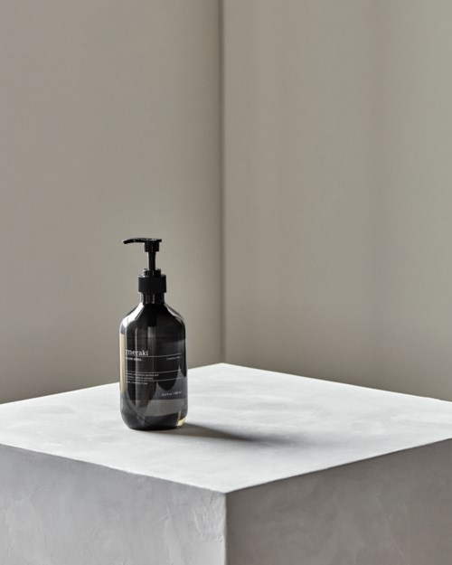 Eine schwarze Seifen- oder Lotionflasche mit Pumpen steht auf einer weißen Oberfläche in einer Ecke.