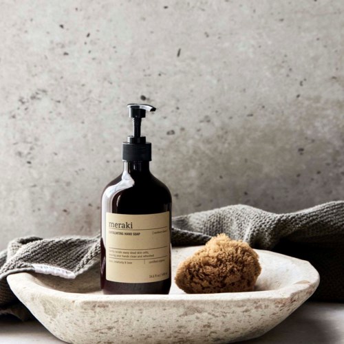 A soap bottle and a sponge on a white tray with a gray cloth, against a plain wall background.