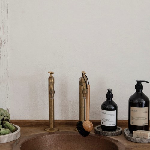 A bathroom sink area with vintage faucet, black bottles, and a wooden brush, all on a wooden counter.