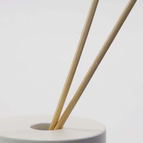 Two bamboo sticks stand in a white holder. The background is plain and light-colored.
