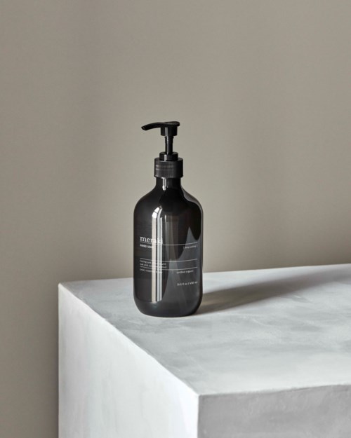 A dark bottle with a pump sits on a white surface, against a plain beige wall.