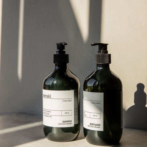 Zwei dunkelgrüne Flaschen mit Pumpaufsätzen, gekennzeichnet für Shampoo und Duschgel, stehen auf einer Oberfläche mit Schatten.