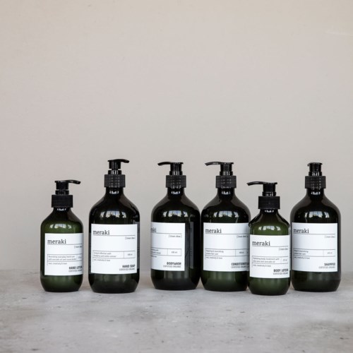 Seven dark bottles with pumps labeled 'Meraki' on a grey surface.