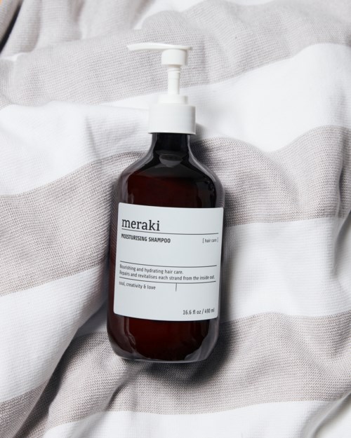 A dark brown bottle with a pump labeled 'Meraki' on a soft, striped fabric.