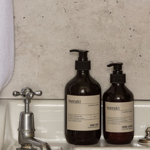 Two dark bottles of hand soap and lotion are on a sink with a gray wall background.