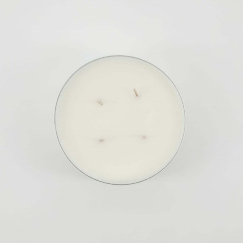 A white candle in a glass container with four burnt wicks, set against a plain white background.