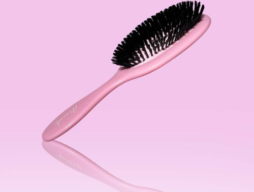 A pink brush with black bristles on a pink background.
