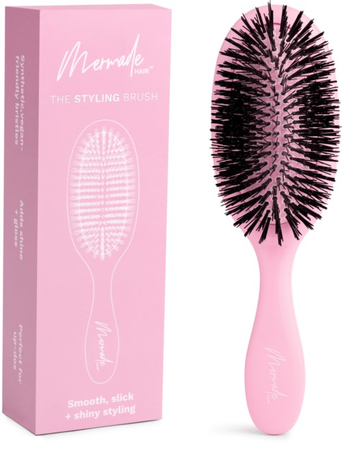A pink hairbrush with black bristles next to pink packaging box, labeled 'Merade hair' and 'styling brush'.