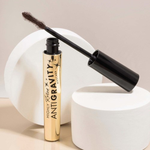 En mascara-rör märkt 'Very Highly Antigravity' med en böjd borste. Den står mellan vita cylindriska former.