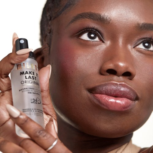 A woman holds a skincare product close to her face, with clear skin and a calm expression.
