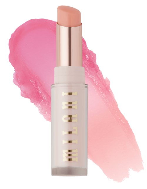 Een roze lippenstift met zachte textuur, in een witte tube met gouden letters, tegen een roze make-up vlek.