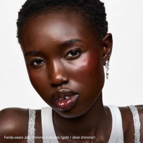 Een vrouw met donkere huid en natuurlijk haar, draagt zilveren oorbellen en een top. Ze heeft glanzende lippen en stralende huid.