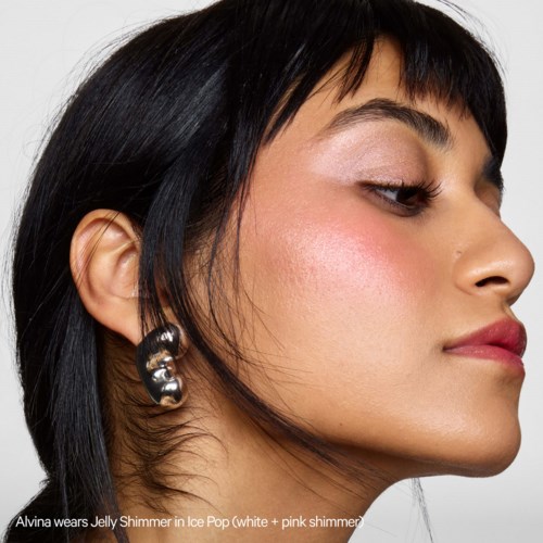 Een vrouw met donkere haren en oorbellen draagt make-up en glanzende lippenstift, kijkt zijwaarts met zelfverzekerde uitdrukking.